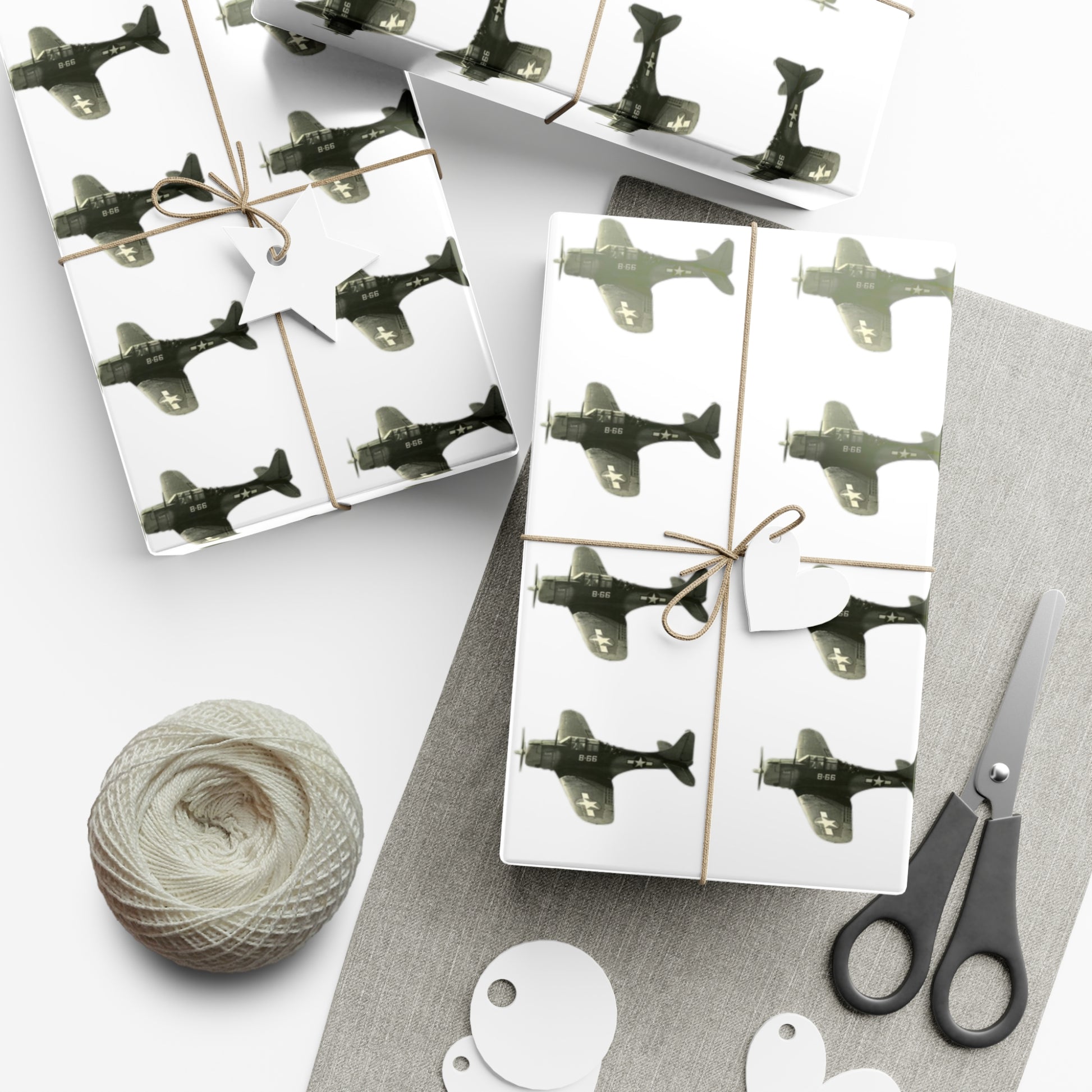 Image is a white work station surface with three gifts wrapped in patterned SBD-Dauntless wrapping paper. The gifts are tired with brown twine. Image also shows a round ball of twine and a pair of scissors. 